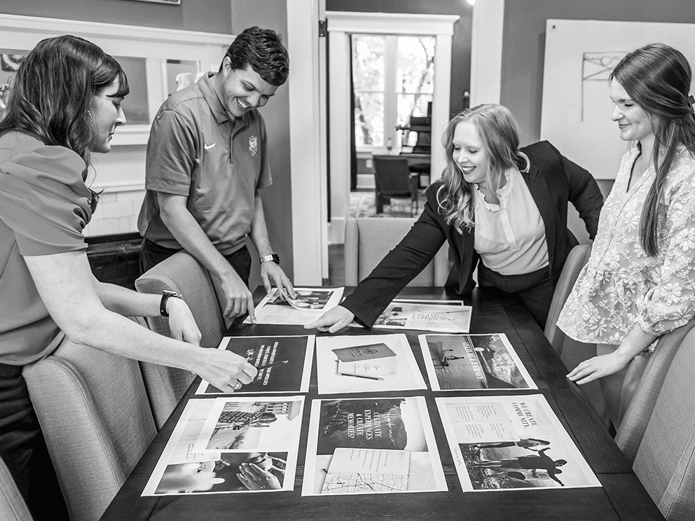 Script Marketing team members standing around a conference table discussing marketing materials for building product industry clients.